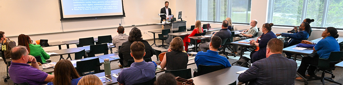 A diverse group of people seated in a classroom, attentively listening to a speaker at the front.