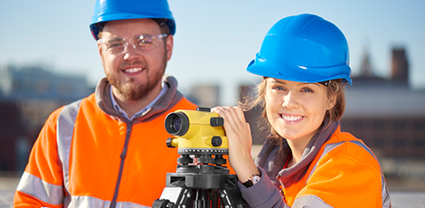 Two people in hard hats and orange reflective jackets standing by a camera