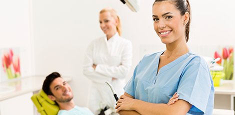 a patient, a dentist, and a dental assistant standing in a dentistry room while smiling.