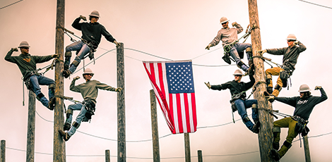 A group of lineworkers stretching an american flag between two telephone poles