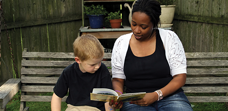 A woman reading to a young boy while sitting on a bench