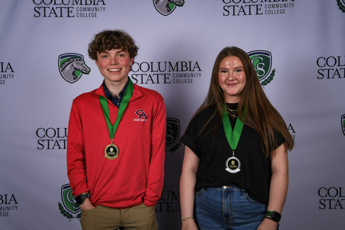 Photo shows a group of three people smiling at the camera with a white background featuring a repeated Columbia State logo pattern.