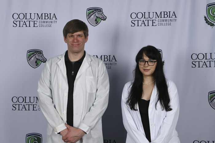 Two people stand in front of a white background.