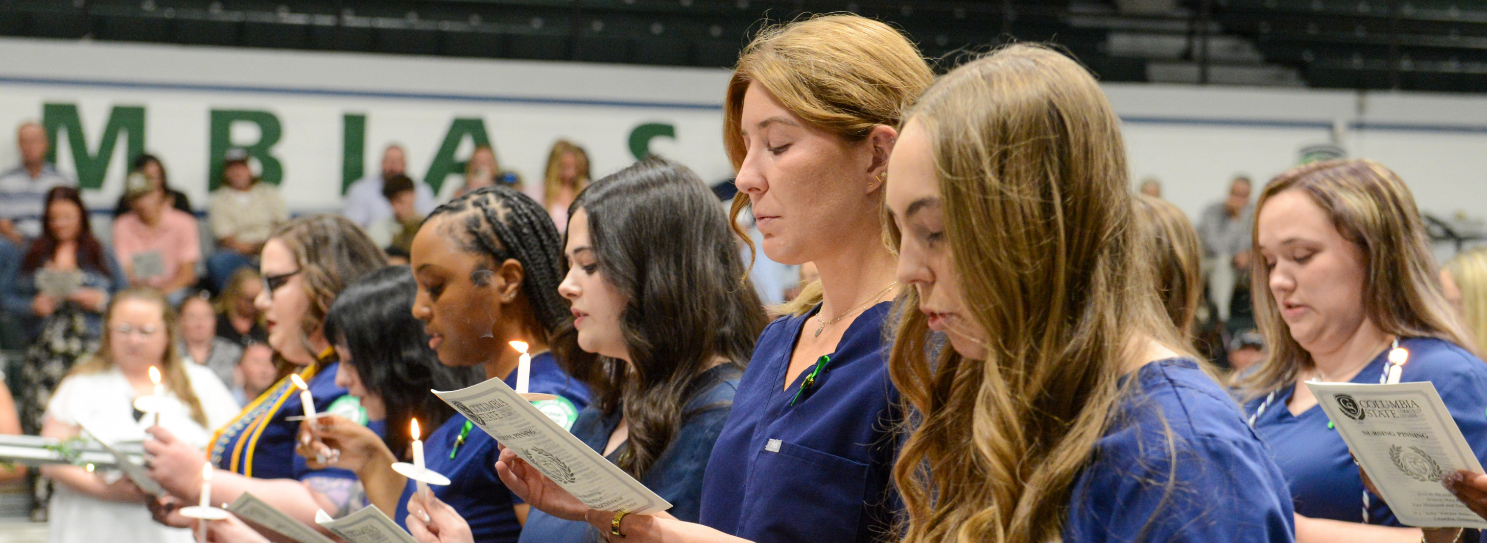A line of people wearing scrubs look down while holding candles.