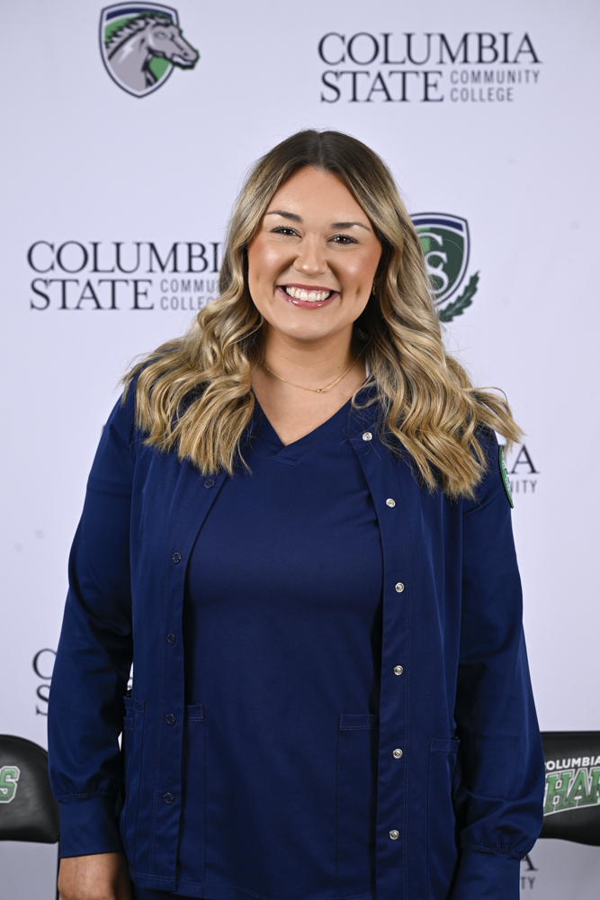 A woman stands in front of a white background.