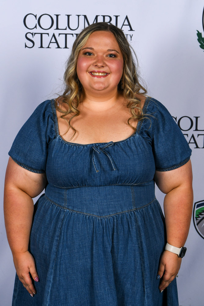 A woman stands in front of a white background.