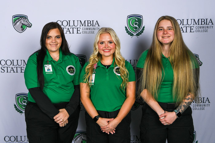 Three of women stand in front of a white background.
