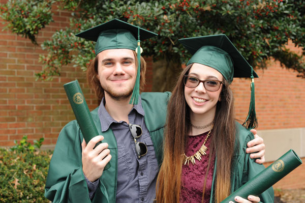 Male and Female graduate in front of tree